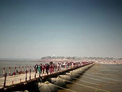 In one direction pilgrims slowly cross long pontoon bridge away from densly crowded Kumbh Mela far river bank.  Ganges, India Stock Footage