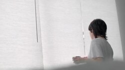 Young woman gets out of bed with cup of coffee, gazes out hotel window, and smiles back at bed Stock Footage