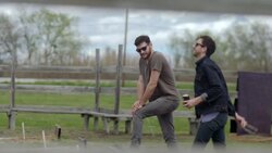 Young man tosses horsheshoe and laughs as friend watches Stock Footage