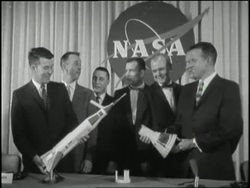 Seven astronauts pose beside a model of the Mercury 7. News Clip