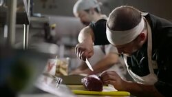 Restaurant chef carefully cuts tuna steak on chopping block in busy kitchen restaurant Stock Footage