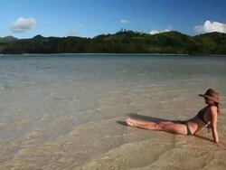 WS, beautiful caucasian woman in bikini relaxing in the sun while sitting in shallow tropical waters with island background / Bacuit Archipelago, El Nido, Palawan, Philippines Stock Footage