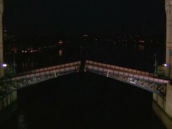 High angle wide shot of person running on Tower Bridge as it raises over the Thames / zoom out to reveal towers supporting bridge / night / London Stock Footage