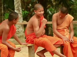 MS SLO MO Shot of three novice monks sitting on bench one of them checking his muscles / Mountain village near Muang Ngoi, Luang Prabang, Laos Stock Footage