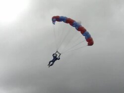 A paraglider drifts through the sky and lands on the ground. Stock Footage