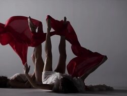 two woman laying on ground with there legs up draped with red silk around them Stock Footage