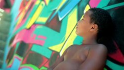 Brazilian boy turns and looks at camera leaning against graffitied wall in Rio slum Stock Footage