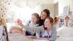 Smiling teenage girls taking selfie with camera phone on bed Stock Footage