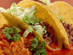 CU PAN across two hard shell tacos with beans and rice on dinner plate as lettuce and shredded cheddar cheese are sprinkled over taco shells Stock Footage