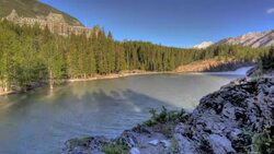 Time-lapse and slide left of river waterfall with mountains and hotel in the background. Stock Footage