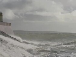 Rough, stormy sea with large waves breaking against sea wall topped by lighthouse, Porthcawl, Wales Stock Footage