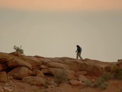 Female hiker silhouetted along red rock ridge in desert Stock Footage
