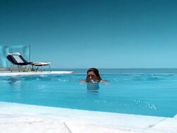 Medium shot woman swimming to edge of pool and smiling at CAM w/beach chairs in background Stock Footage