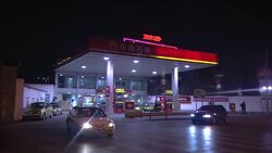 Vehicles drive away from a gas station at night as fireworks explode overhead. Stock Footage