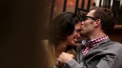 Hip young man kisses girlfriend on forehead, girl leans in to whisper in his ear; people crossing in foreground (dolly-shot) Stock Footage