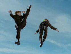 Wide shot two business men in midair after jumping on trampoline, with one nearly kicking other's head in midair Stock Footage
