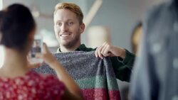 Young man holds up sweater and poses for smartphone photo in trendy clothing shop Stock Footage