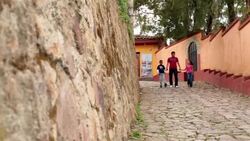 Hispanic teenage brother walks hand-in-hand with younger siblings down third-world street (dolly-shot) Stock Footage