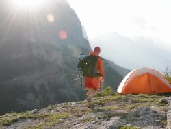 Woman stands beside tent pitched on mountain ridge crest Stock Footage