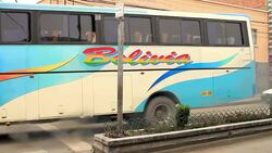 A brightly colored Bolivian bus drives in traffic in front of graffiti-defaced shops. Stock Footage