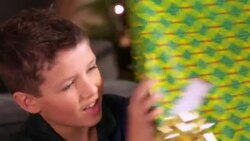 Young boy shakes present intently in front of Christmas tree Stock Footage