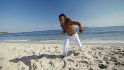 Capoeira artist on Ipanema Beach runs and jumps into flying punch towards camera Stock Footage