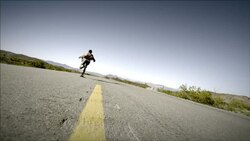 Young skater speeds down empty desert road on skateboard (slow-motion) Stock Footage