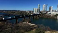 Train Crosses The Colorado River across Town Lake in Austin , Texas with Downtown Condos on the North Side and Texas Hill Country in the Background Stock Footage