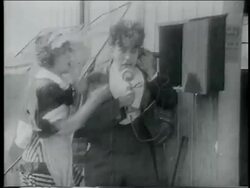 B/W 1915 woman (Mable Normand) grabbing telephone from man (Charlie Chaplin) + talking into it Stock Footage
