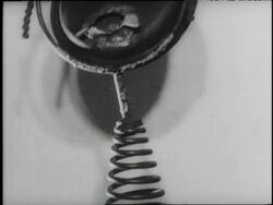 A sculptured metal face sits atop a large metal spring News Clip