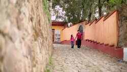 Hispanic brother and sister hold hands walking down third-world street; brother points something out (dolly-shot) Stock Footage
