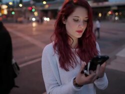 Woman standing at busy intersection in Berlin, Germany, going through online dating profiles on mobile phone, laughing in evening Stock Footage