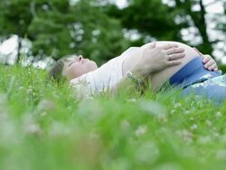 MS Pregnant woman lying in grass gently rubbing her abdomen / West Hurley, New York, United States Stock Footage