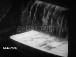 1952: JONES AND LAUGHLIN STEEL COMPANY:  VS Slab of glowing steel, burning, moving down rollers in steel mill, slabs moving through liquids, factory worker operating machine pouring liquid metal into thimble from blast furnace. J&L Coal Instructional Video