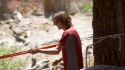 A man and woman setting up a slackline between two trees in the wilderness. Stock Footage