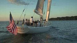 An American flag blows in the wind on the stern of the sailing yacht Heroina in Narragansett Bay at sunset. Stock Footage