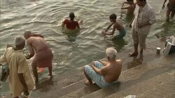 A devotee dips an urn and a seashell into the Ganges as other devotees bathe or wait their turns. Stock Footage