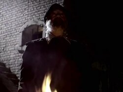 A fire burns below a man in period clothing near a brick wall. Stock Footage