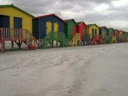 Tracking shot along the beach with colourful change rooms and a single deck chair Stock Footage