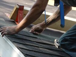 MS SLO MO Worker positioning shingles and hammering on roof of red building / Chelsea, Michigan, United States Stock Footage