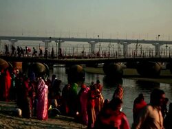 Colorful sari-clad figures crowd riverbank in early morning sunshine preparing to bathe in the Ganges. Kumbh Mela, India Stock Footage