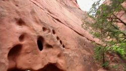 Tilt down to young boy in red-rock shallow cave smiling in hiking attire (close-up) Stock Footage