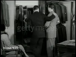 1950: NEW YORK CITY:  EXT Rogers & Peet clothing store w/ people walking sidewalk. DRAMATIZATION: Male  trying on suit, wife sitting in chair shaking head, male in another suit saying he likes it, wife saying they'd like to see something else. Instructional Video