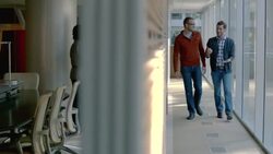 Male and female business partners write on white-board, two trendy businessmen discuss strategy with tablet as they walk up office hallway (dolly shot) Stock Footage