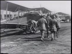 1917: WWI US PILOTS TRAINING: KELLY FIELD: WS Line of cadets, singles walking, saluting. VS Cadets & pilots to Curtiss JN-4 'Jenny' training biplane, getting into aircraft, into helmet, goggles. VS Three men trying to turn propeller, several tries. Instructional Video