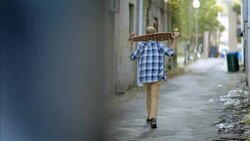 Young man walks up urban alley carrying longboard over shoulder Stock Footage