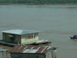 View of a typical wooden house at amazon river with a outboard-motor boat crossing behind it - landscape view Stock Footage