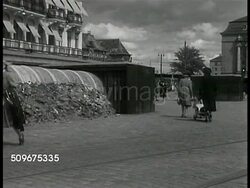 1943: STOCKHOLM, SWEDEN: WS Air Raid shelter (above ground tunnel & boxes) in front of building, people riding bicycles FG. Women walking past Air Raid shelter. VS People riding bicycles on street w/ trams, few cars.  Fuel shortage, WWII. Instructional Video