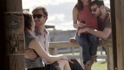 Young couple sit and kiss on wooden fence in Texas ghost town while friends look at smartphone Stock Footage