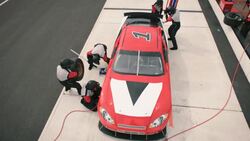 Red race-car pulls into pit-road, pit-crew leaps into action Stock Footage